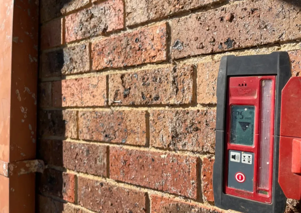 Red fire alarm on cracked weathered brick wall showing rising damp issues.